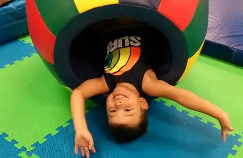 Kid rolling around on floor in play equipment at Children's Therapy Program Easter Seals Greater Houston