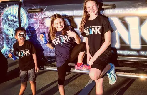 Three kids leaning up against THINK Institute truck; pediatric neurology