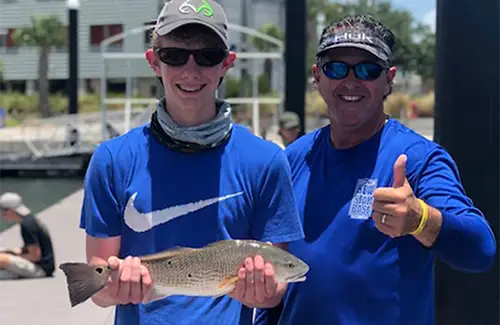 teen holding fish he caught next to his father standing on dock in Galveston