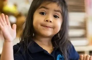 Little girl waving and smiling at The Children's Courtyard; daycare summer camps
