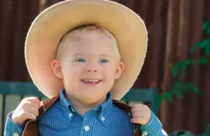 Young kid with down syndrome wearing a cowboy hat and smiling for picture