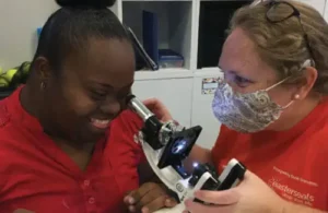 Student with Down Syndrome looking through microscope with teacher assistance at Easter Seals Greater Houston The Caroline School; down syndrome and autism