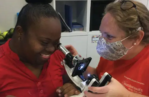 Student with Down Syndrome looking through microscope with teacher assistance at Easter Seals Greater Houston The Caroline School; down syndrome and autism
