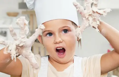 young chef with food on her fingers and hands raised