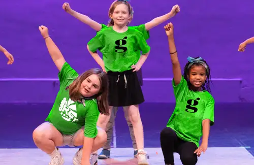 Group of kids performing on stage with purple lit background at A.D. Players Summer Theatre Camp.