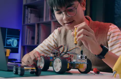 Kid sitting at desk building a small robotic car at Learn to Bot; coding robotics summer camp.