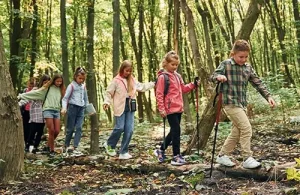 Woodlands Forest School student group walking through a forest area with walking sticks.