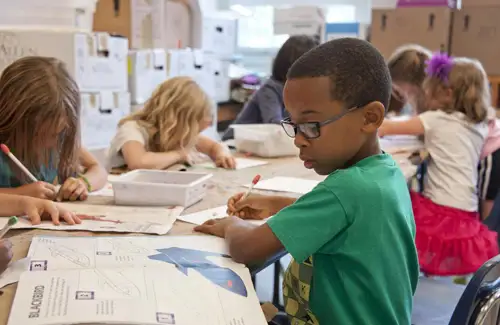 Academic tutoring and homeschool program student doing schoolwork at table with other kids at Children Come Click