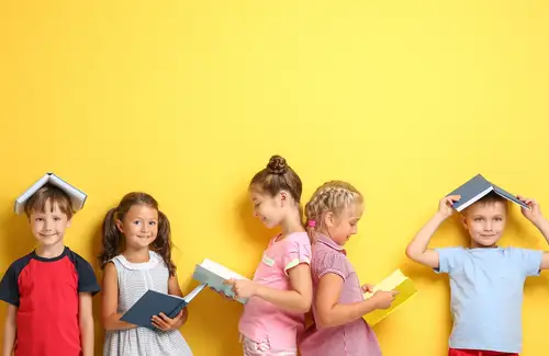 Children posing in different ways with books in hand against a yellow wall.