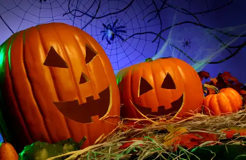Pumpkin Jack-O-Lanterns with scary faces carved into them sitting on hay.