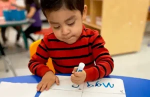 Young student sitting at a desk writing on paperwork at Laugh N Discover.