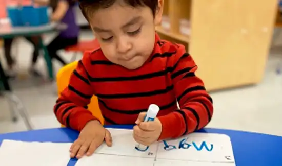 Young student sitting at a desk writing on paperwork at Laugh N Discover.