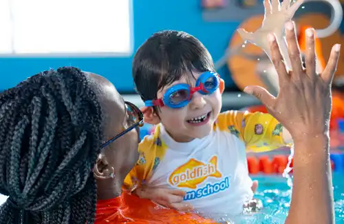 Swim student giving a high-five to instructor for a great job at Goldfish Swim School.