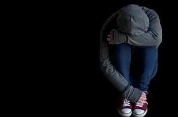 Social Media Impact On Mental Health In Teens blog article image. Depressed teen sitting on black background.