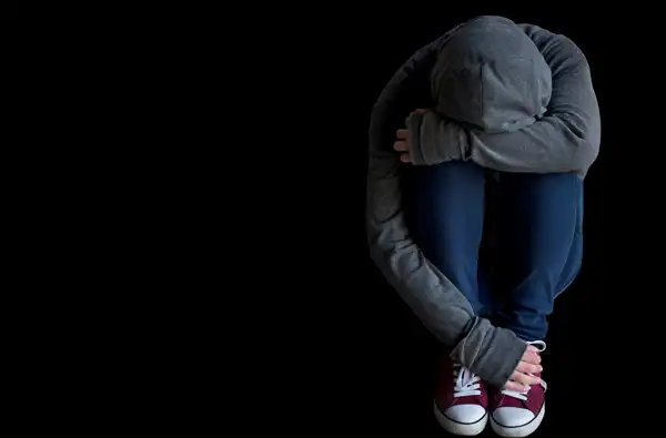 Recognizing The Negative Impacts Of Social Media On Teens: A Comprehensive Overview blog article image. Depressed teen sitting on black background.
