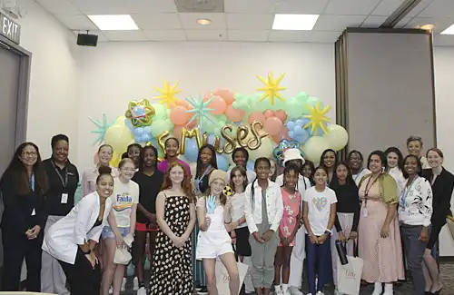 STEMuses Empower HER Summit 2025 group of kids gathered together in front of a balloon background