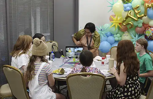 Kids sitting around a table work on a STEM project with instructor at STEMuses.