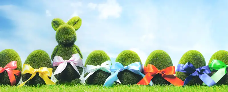 Green grass hedges in the shape of eggs and a bunny with different color ribbons for Easter blog article image.