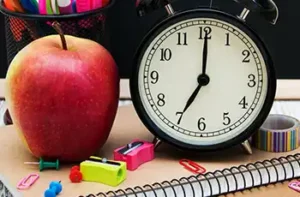 How to Survive School Mornings With Toddlers and Preschoolers main blog image showing school supplies, a clock, and an apple on a desk; school year survival tips for parents.