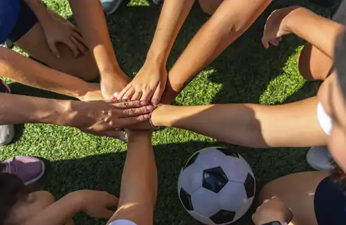 Texas A&M Aggie Overnight Soccer Camp - Texas A&M Aggie Soccer Camp; soccer group with all hands in the middle with soccer ball below.