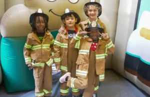 Four kids dressed in fireman outfits at birthday party at the Houston Fire Museum.