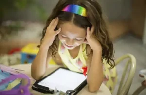 Read-A-Rific; young child sitting at small table looking at glowing tablet.