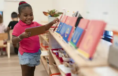 Child smiling big at Bezos Academy while retrieving a book from the bookshelf.