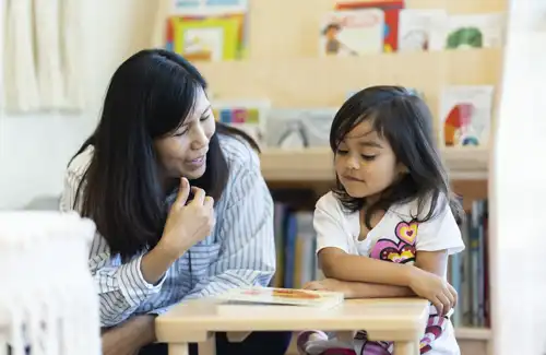 Teacher at Bezos Academy helping child with a book. Bezos Academy Free Montessori Preschool