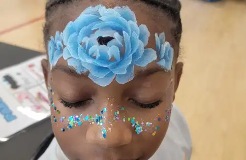Face painting of blue and white flowers across the forehead with some sparkles and dots across the cheeks and nose by Texas Fun Face Painting.