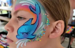 Face painting of a dolphin splashing with some sparkles by Texas Fun Face Painting. Texas Fun Face Painting and Balloon Art