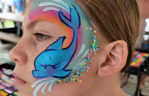Face painting of a dolphin splashing with some sparkles by Texas Fun Face Painting. Texas Fun Face Painting and Balloon Art