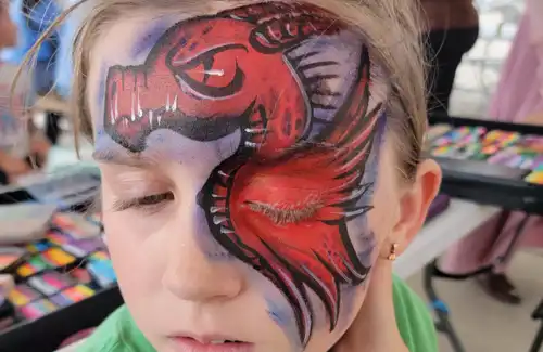 Face painting of a big red dragon covering one eye by Texas Fun Face Painting.